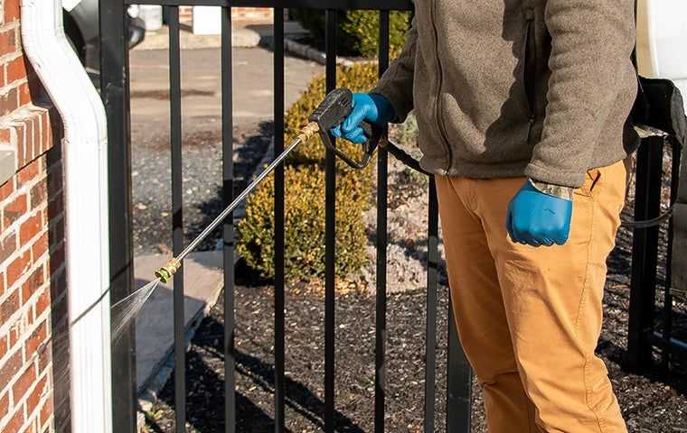 Applying a liquid spray barrier around the exterior walls, windows, and doors of a home for pest control