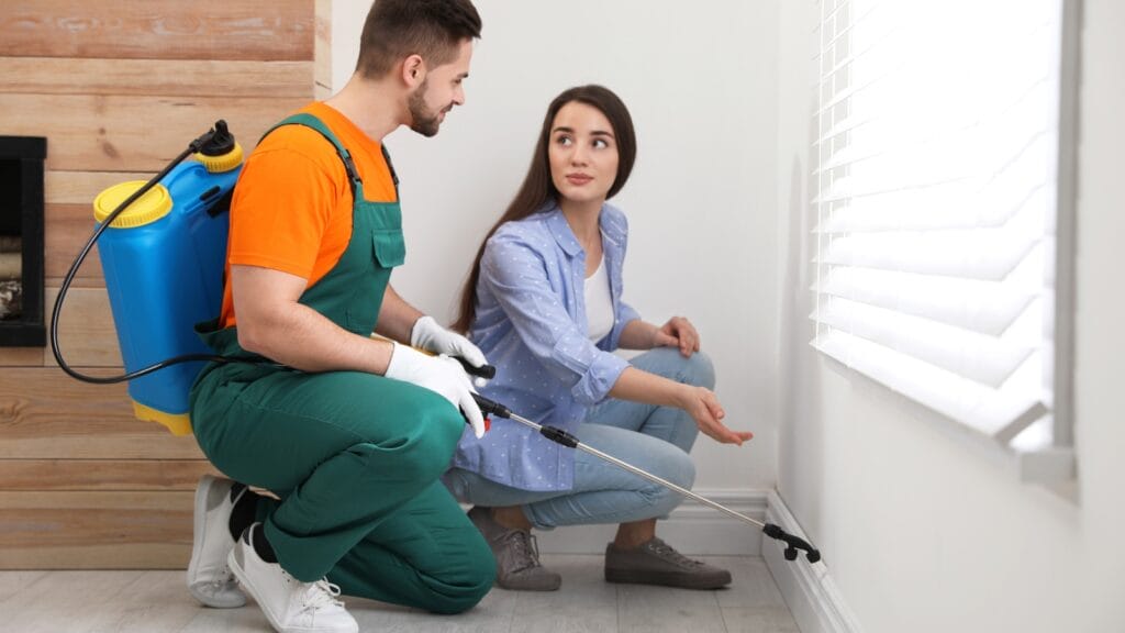 A worker in gloves uses a caulk gun to seal a window frame, blocking gaps where pests could enter a home.
