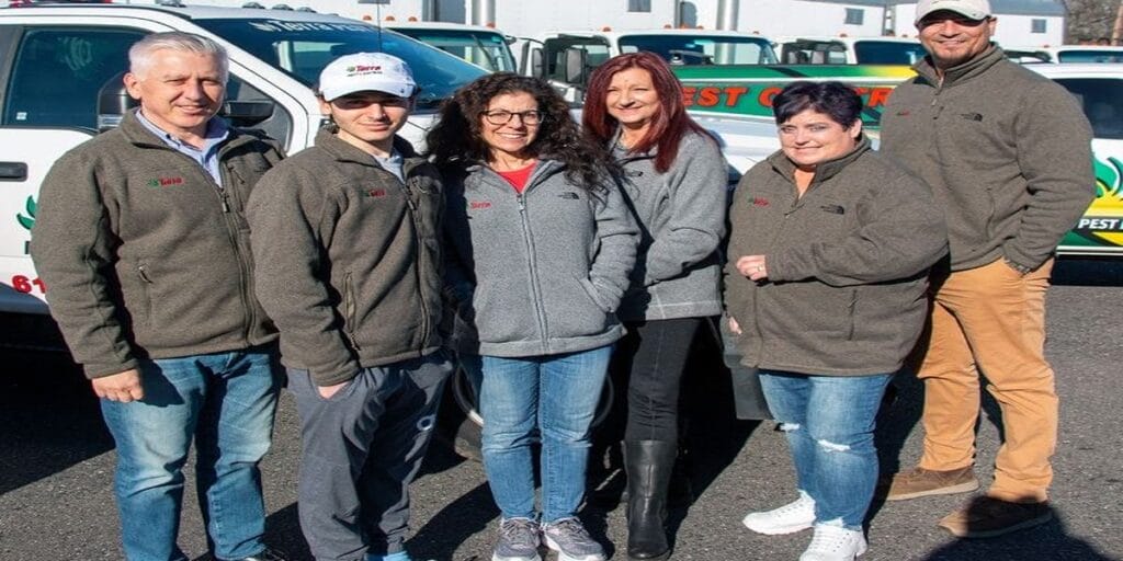 Six members of the Terra Pest Management team stand together in a parking lot in front of their service trucks.